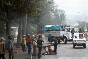 Arbeiter führen Aufgaben neben einer Straße mit einem Lkw aus, der eine große Menge trägt, während Beamte in einem Fahrzeug in der Nähe fahren, umgeben von Bäumen und Straßenlaternen.