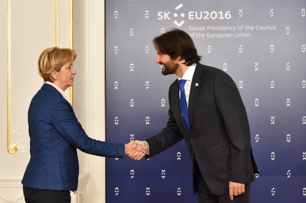 Bundeskanzlerin Angela Merkel und Bundespräsident Joachim Gauck schütteln sich die Hände vor einer Wand mit einem "EU-Gipfel"-Banner und einer Tür im Hintergrund, beide lächeln.
