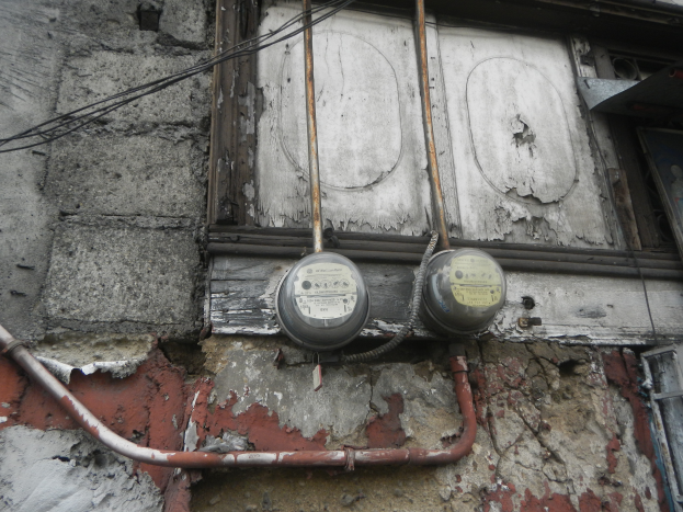 Ein altes, baufälliges Gebäude mit abblätternder Farbe und bröckelnden Wänden, das zwei angebrachte Meter, verschiedene Rohre und Drähte aufweist.