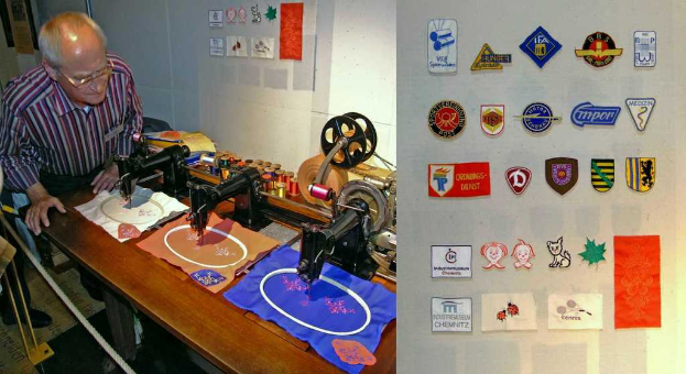 Ein Mann mit Brille steht hinter einem Tisch mit Nähmaschinen, Kleidung und einer Tafel mit einigen Abzeichen, mit verschiedenen farbigen Fäden im Hintergrund.