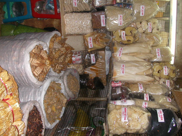 Ein Marktstand mit ordentlich sortierten Lebensmitteln in Tüten und Plastikabdeckungen auf Gestellen.