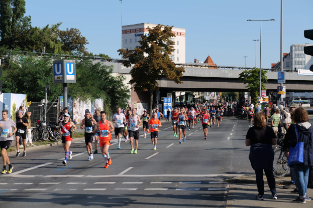 Gruppe von Menschen, die bei einem Marathon auf einer baumbestandenen Straße unter einem klaren blauen Himmel laufen.