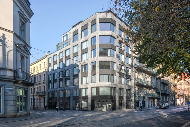 Großes Bürogebäude mit vielen Fenstern, umgeben von Straßeninfrastruktur, Fahrzeugen, Fußgängern, Bäumen und einem bewölkten Himmel.