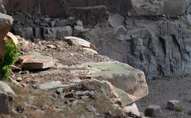 Eine felsige Anhöhe mit einer markanten Felsformation in der Mitte, umgeben von Gras und kleinen Pflanzen.
