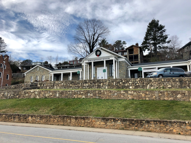 Steinwand mit parkenden Autos, benachbarten Gebäuden mit Fenstern und Türen, Bäumen und einem bewölkten Himmel im Hintergrund, als das kürzlich wiedereröffnete Weltkulturerbe-Museum bezeichnet.