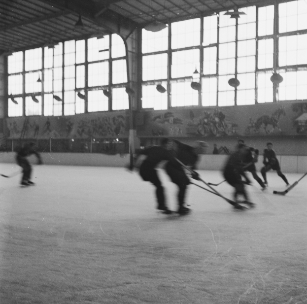 Schwarzes und weißes Foto von Menschen, die Hockey auf einem Eisplatz spielen, mit Gemälden und Fenstern auf der Hintergrundwand.