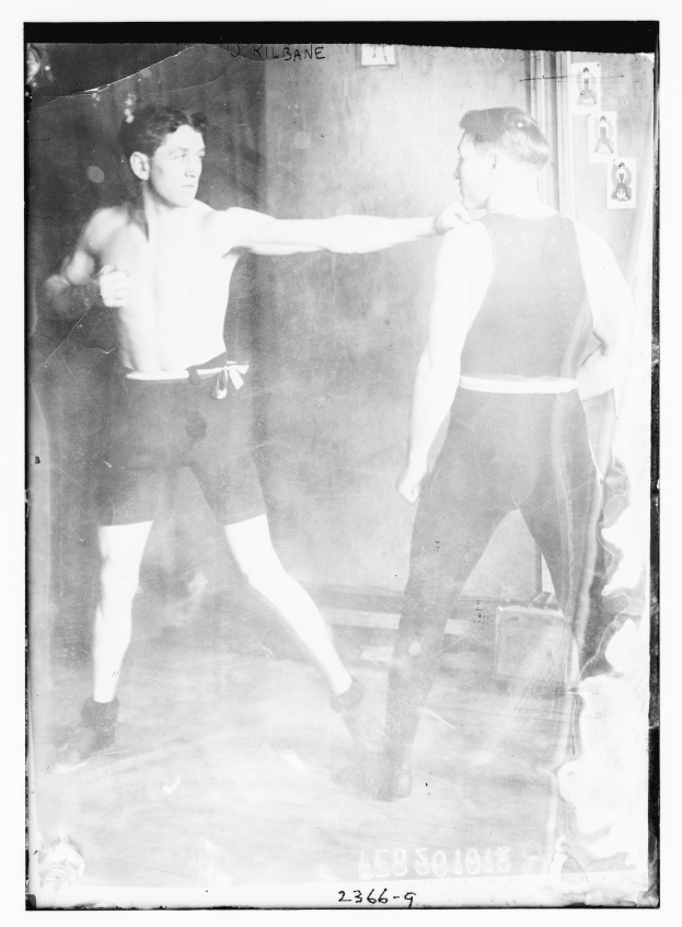 Schwarzes und weißes Foto von zwei Boxern in einem Boxring mit Postern an der Hintergrundwand und Text unten.