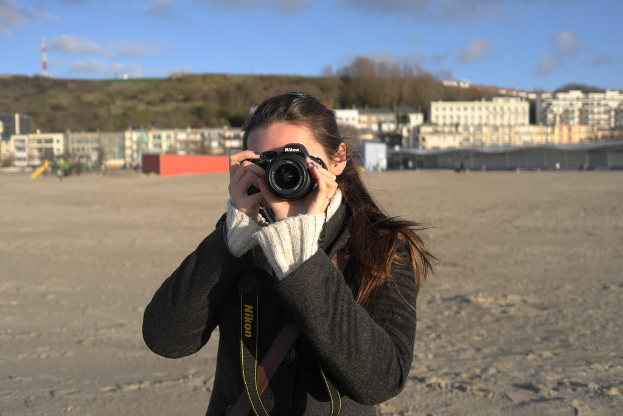 Eine Frau mit einer Kamera vor einem Hintergrund aus Geb√§uden.