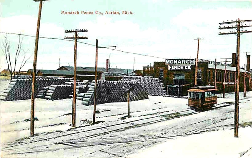 Eine schneebedeckte Landschaft mit einem auf einer Spur fahrenden Fahrzeug, umgeben von Pfählen, und einer Sammlung von Gegenständen hinter den Pfählen sowie einem Fabrikgebäude im Hintergrund.