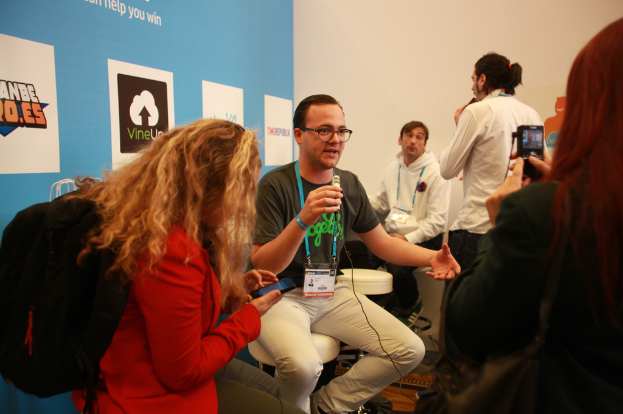 Ein Interview-Szenario mit Menschen mit Mikrofonen und einer Kamera, ein Banner auf der linken Seite und Menschen in der vorderen und mittleren Ebene, mit einem klaren Hintergrund.