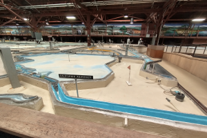 Ein großes Indoor-Wasserpark mit zahlreichen Wasserrutschen, Pfosten, Texttafeln, Deckenleuchten und Wandgemälde, das einem Minigolfplatz ähnelt und für einen spaßigen und aufregenden Erlebnis bietet.