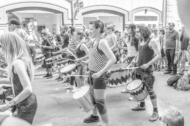 Eine Gruppe von Menschen spielt draußen auf Musikinstrumenten in der Nähe einer geschlossenen Glastür mit einer Leuchte im Hintergrund.