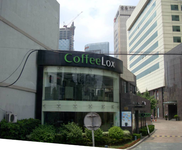 Ein Geschäftsgebäude mit einigen Pflanzen davor, umgeben von vielen hohen Gebäuden im Hintergrund, mit einigen Drähten sichtbar.