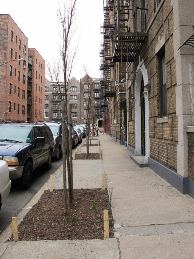 Eine spärlich bebaute Szenerie mit wenigen Autos und Gebäuden im rechten Eck und einigen anderen Gebäuden im linken Eck.