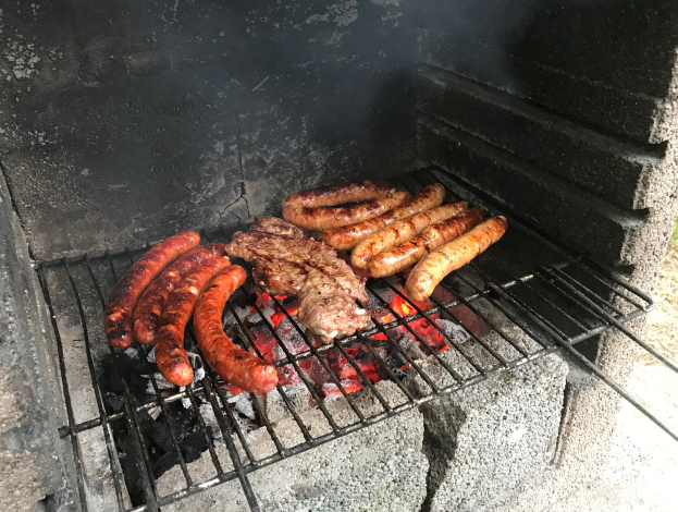 Grill mit Würstchen und Fleisch über Kohle und Feuer, auf Gras im Freien