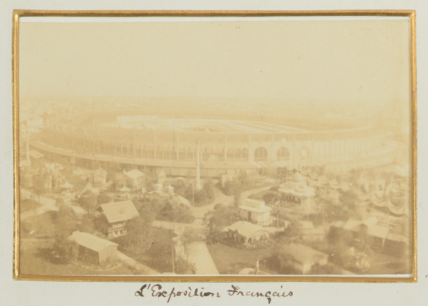 Altes Foto eines Stadions in einer städtischen Umgebung mit umliegenden Gebäuden, Bäumen und Pfählen, mit Text am unteren Rand.