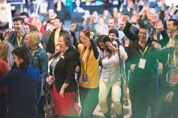 Eine Gruppe von Menschen, die lachend mit einem Mikrofon auf einem Ständer in der Mitte stehen.