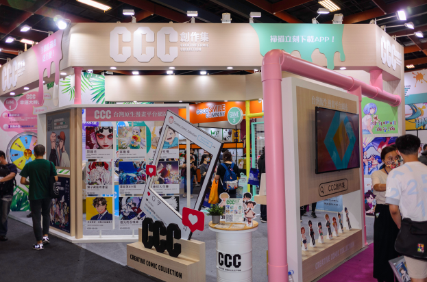 Eine Gruppe von Menschen steht vor einem Messestand, der mit Plakaten, einem Fernseher und Deckenleuchten geschmückt ist.