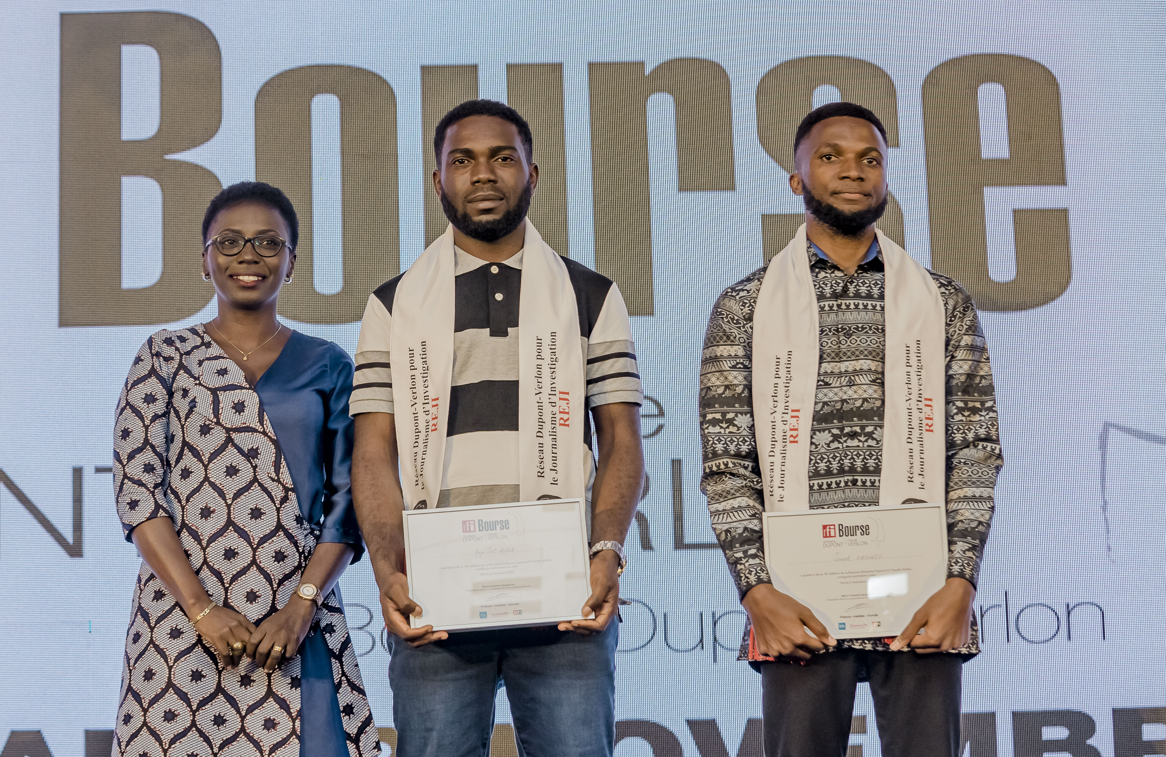 Drei Menschen stehen nebeneinander auf einer Bühne, jeder hält ein Zertifikat in der Hand, im Hintergrund ist ein Bildschirm mit der Aufschrift "Bounce Africa Awards 2019".