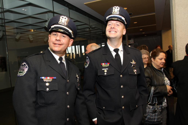 Zwei strahlende Beamte vorne, Menschen in der Mitte, Glasfenster links, Lampen und Decke oben und Säulen und Menschen rechts.