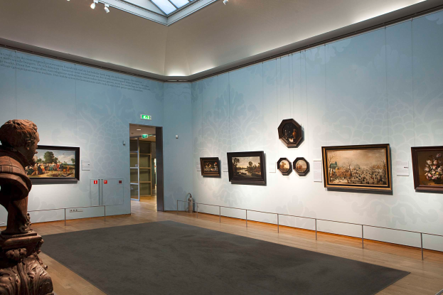 Ein prächtiger Museumsraum mit einer Statue links, einem Teppichboden, Fotorahmen an den Wänden, einer Glasdecke mit Lampen und Türen im Hintergrund.