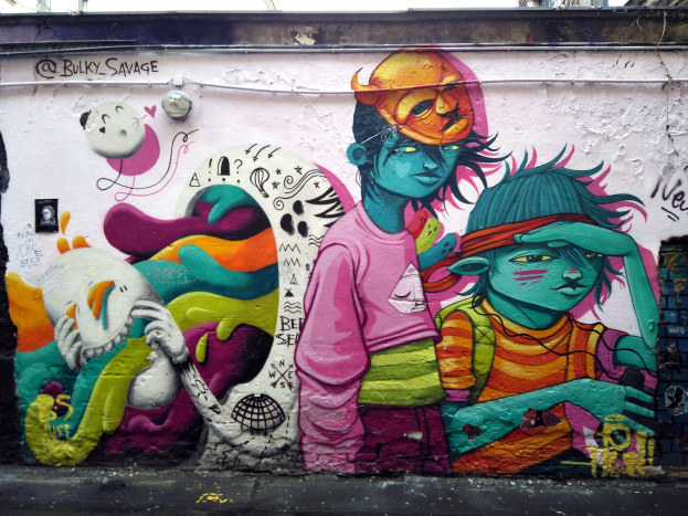 Mural an einer Gebäudewand mit Graffiti, das eine Straße am Boden, Strommasten und einen klaren blauen Himmel im Hintergrund zeigt.