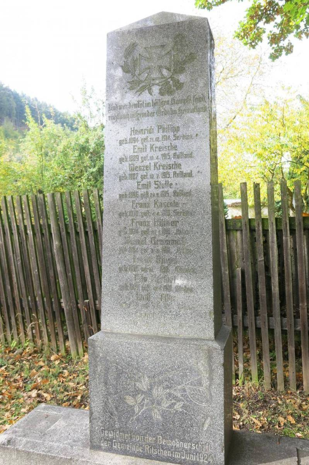 Ein Denkmal auf einem Friedhof für deutsche Soldaten, die im Zweiten Weltkrieg starben, mit einem Holzzaun, Bäumen und einem klaren Himmel im Hintergrund.