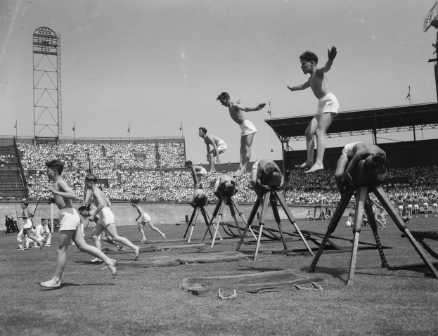 Schwarzes Bild von jungen Männern, die Hürden in einem Stadion mit Zuschauern auf den Rängen überspringen.