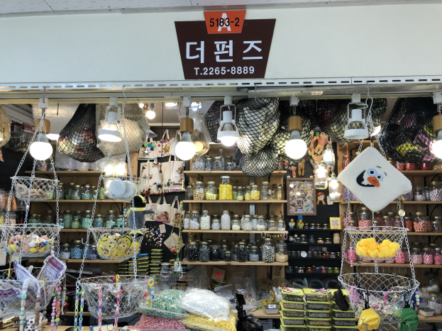 Ein unordentlicher Laden in Seoul, der verschiedene Gegenstände wie Körbe, Lampen, Flaschen und Spielzeuge auf Regalen anbietet, mit einem Schild oben, das darauf hinweist, dass es einer der besten koreanischen Läden ist.
