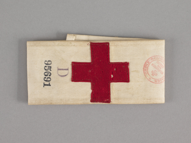 Ein rotes Kreuz-Ersthilfekit in einer Stofftasche mit Text und einem Stempel, das auf einer Oberfläche liegt.