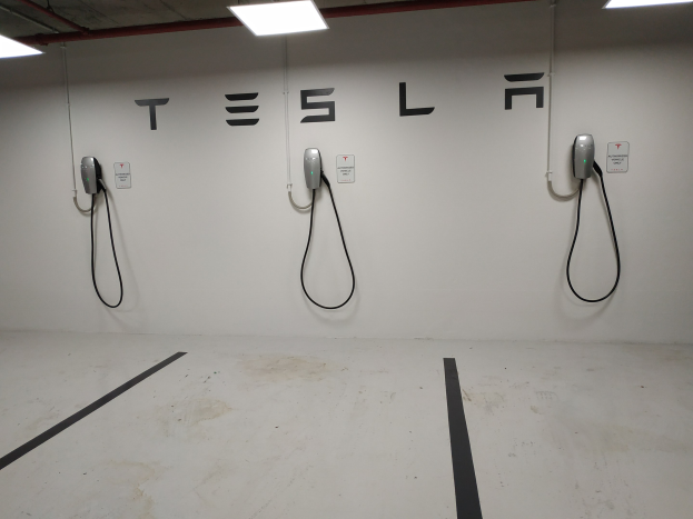 Eine Tesla-Ladestation in einer Tiefgarage mit an der Wand angebrachten Kabeln und Deckenbeleuchtung, die die darunterliegende Etage zeigt.