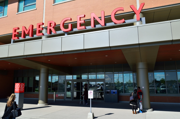 Eine Gruppe von Menschen geht auf ein Notaufnahmelager mit Glaswänden, Säulen, einem Namensschild, Hinweistafeln und einem Abfalleimer zu.