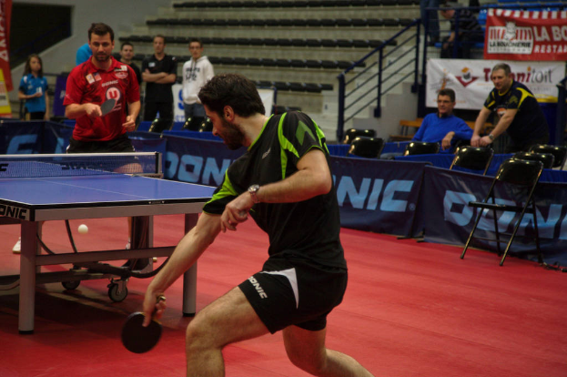 Eine Gruppe von Menschen in verschiedenen Farben, darunter schwarz, weiß und blau, versammelt sich um einen Tisch mit einem Spiel in Arbeit, mit Stühlen und einer Treppe im Hintergrund.