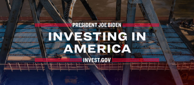 Präsident Joe Biden neben einer Brücke mit dem Text "In America investieren" im Vordergrund und verstreuten Gegenständen auf dem Boden.