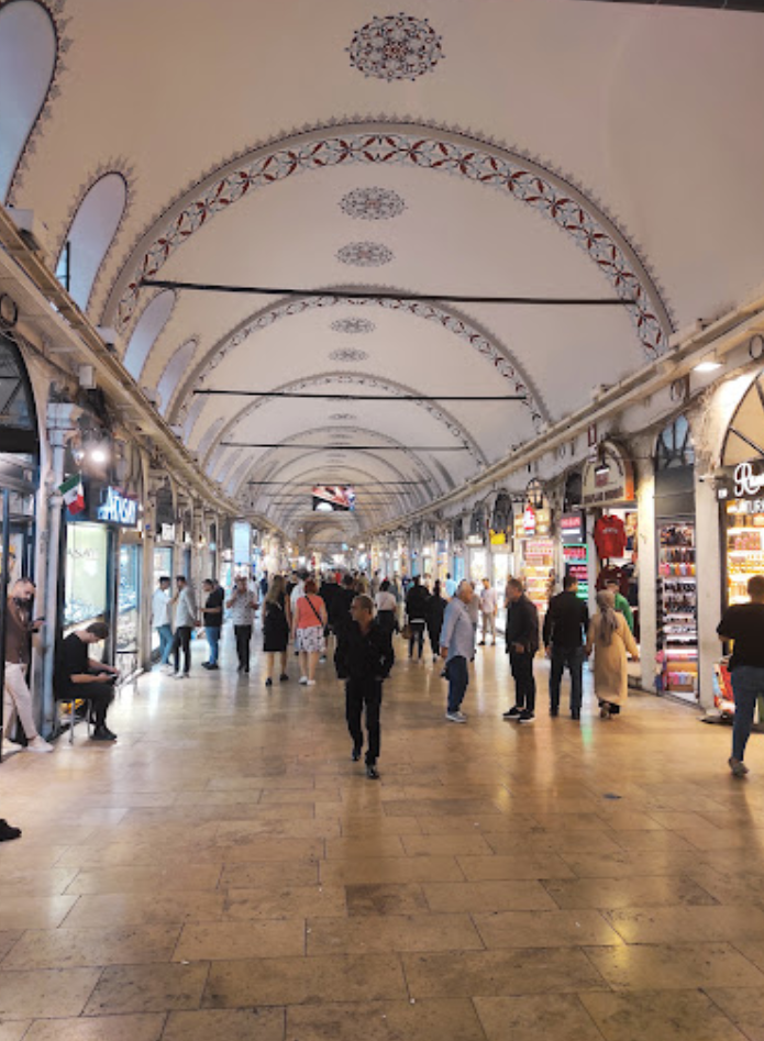 Der Große Basar in Istanbul, Türkei, voller Menschen, die gehen und sitzen, Geschäfte auf beiden Seiten und eine kunstvoll gestaltete Decke.
