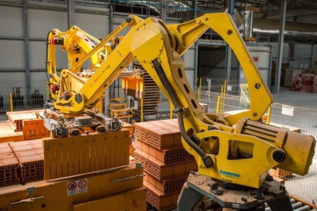 Großes Industriegelände mit gestapelten Kisten, Kränen, Zaun, Strommasten und einer fernen Wand in einer automatisierten Fertigungsumgebung.