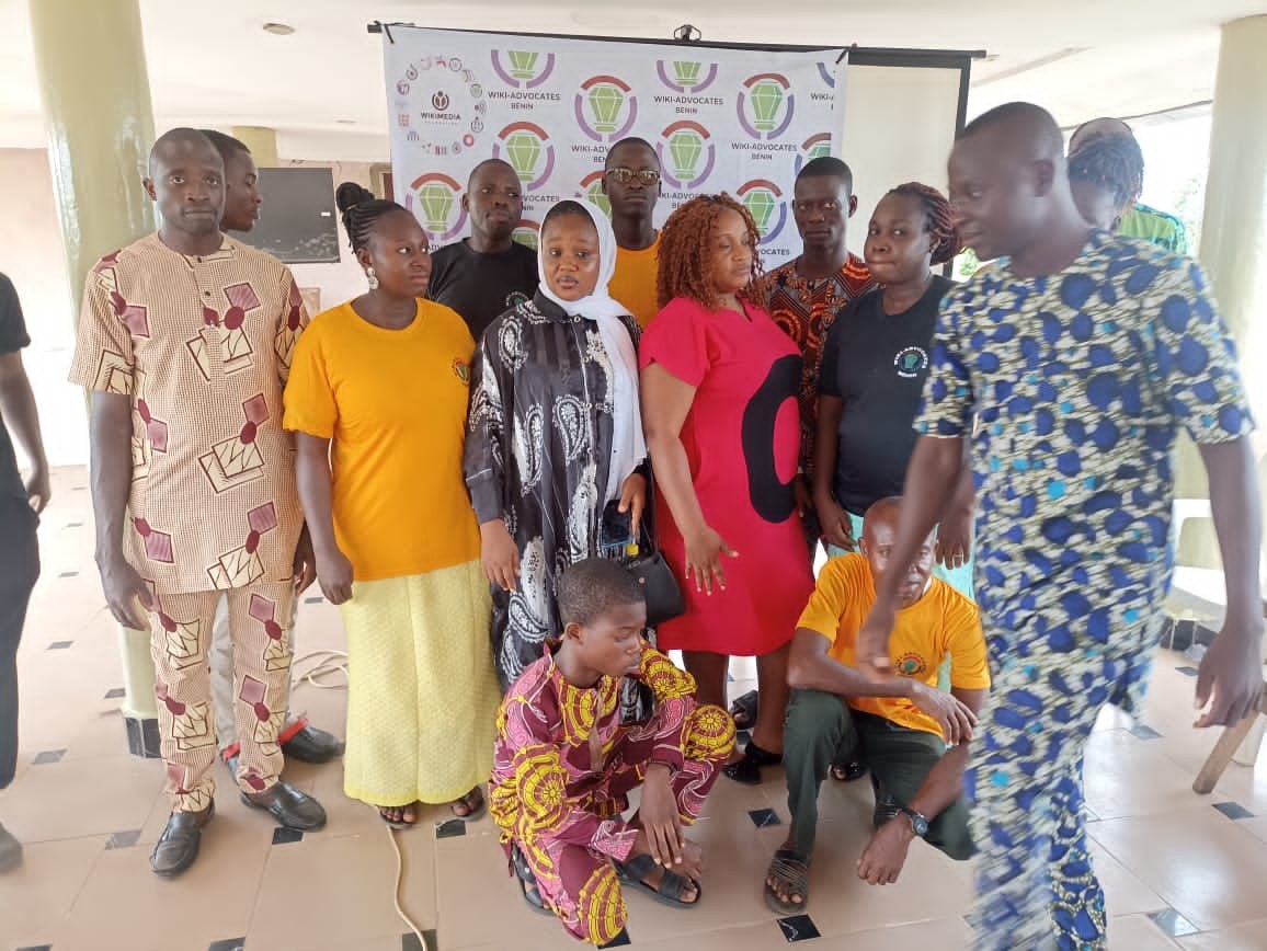 Eine Gruppe von Menschen steht vor einer Fahne mit der Aufschrift "Advocates in Ghana: Ein Schritt-für-Schritt-Führer", mit Stühlen, Säulen, einem Fernseher und Deckenleuchten im Hintergrund.