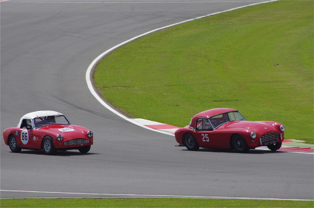 Zwei rote Autos auf einer Rennbahn mit einem Rasenstreifen auf der rechten Seite.