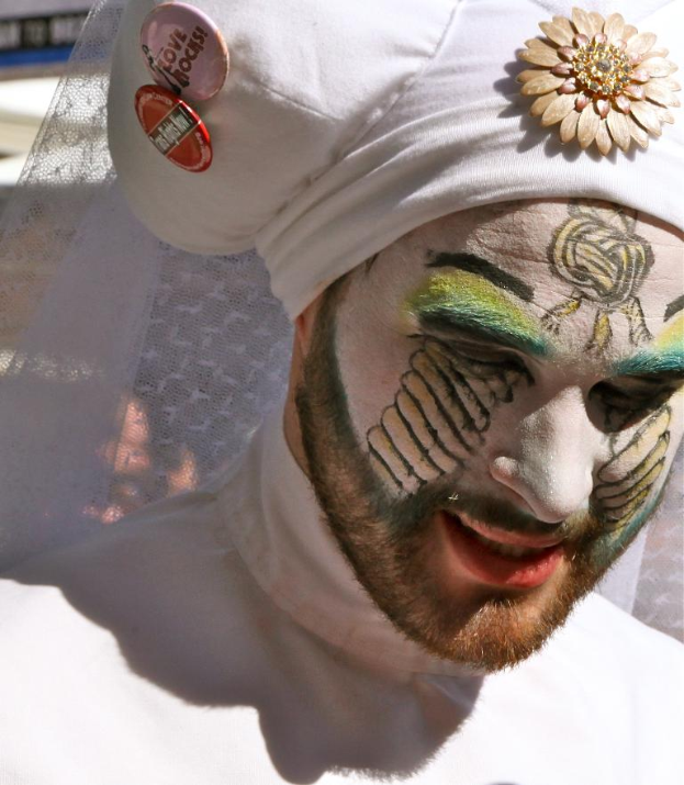 Ein Mann mit Gesichtsschminke und einer Mütze mit Text, der vor einem Tuchhintergrund steht.