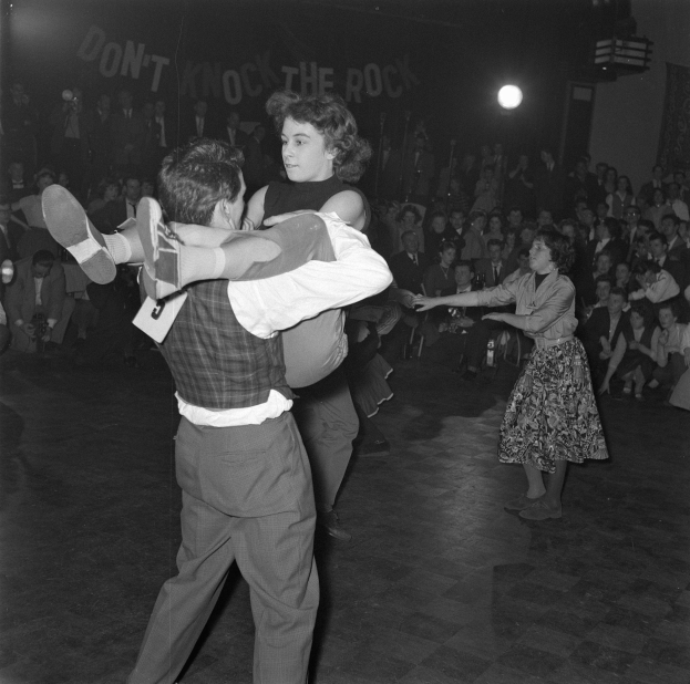 Ein Mann und eine Frau tanzen gemeinsam vor einem Publikum, beleuchtet von einem Licht, auf einem Schwarz-Weiß-Bild.