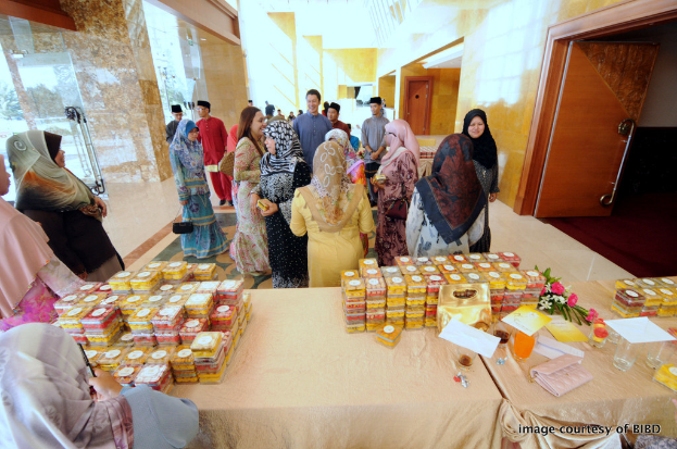 Eine Gruppe von Menschen, die um einen Tisch mit einer Decke, Schachteln, einer Brieftasche, einem Glas, einem Teller und Blumen stehen, mit einer Tür auf der rechten Seite und einer Glastür auf der linken Seite.