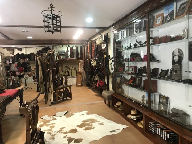 Ein überfülltes Boutique-Zimmer in Barcelona mit einem Kuhfellteppich, hängenden Kleidern, Hüten, gerahmten Fotos und verschiedenen Gegenständen in Schränken, beleuchtet von Deckenlampen und einem Kronleuchter.