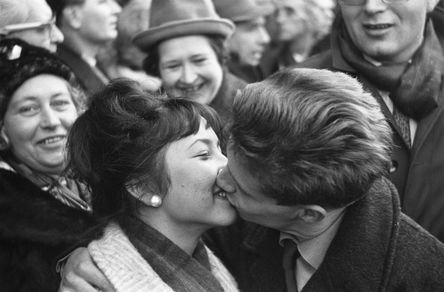 Ein Schwarz-Weiß-Foto eines Mannes und einer Frau, die leidenschaftlich vor einem lächelnden Publikum knutschen.