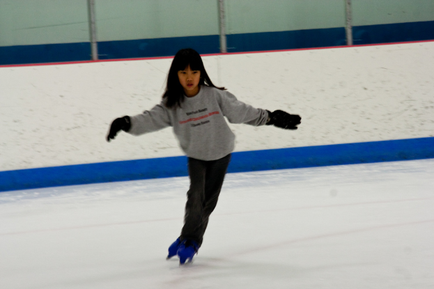 Eine Person in Kleidung fährt auf dem Eis mit Stöcken, die oben im Bild zu sehen sind.