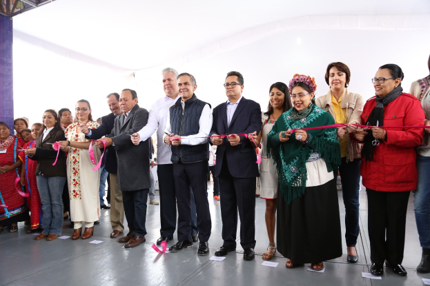 Gruppe von Menschen, die eine Schnur bei einer Zeremonie durchschneiden, vor einer Menge mit Papieren auf dem Boden und einem weißen Tuch im Hintergrund.