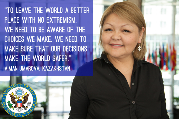 Eine Frau in einem schwarzen Kleid steht vor einem Fenster mit einer Inschrift über die Welt sicherer zu machen, mit Flaggen im Hintergrund.