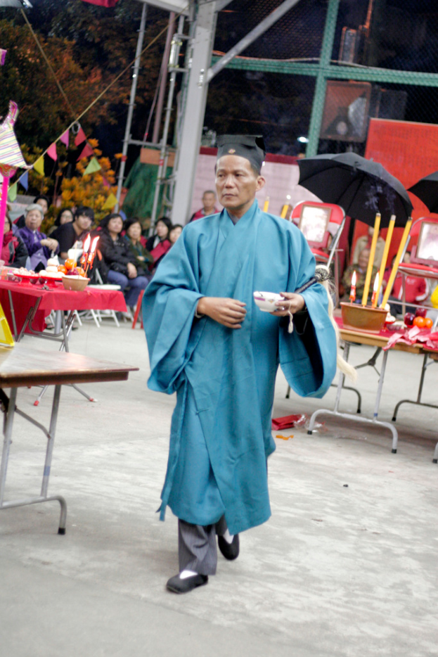 Eine Szene mit Bäumen, ein paar Menschen, einem Schirm und einem Tisch mit einer Kerze, einer Schüssel und Tellern.