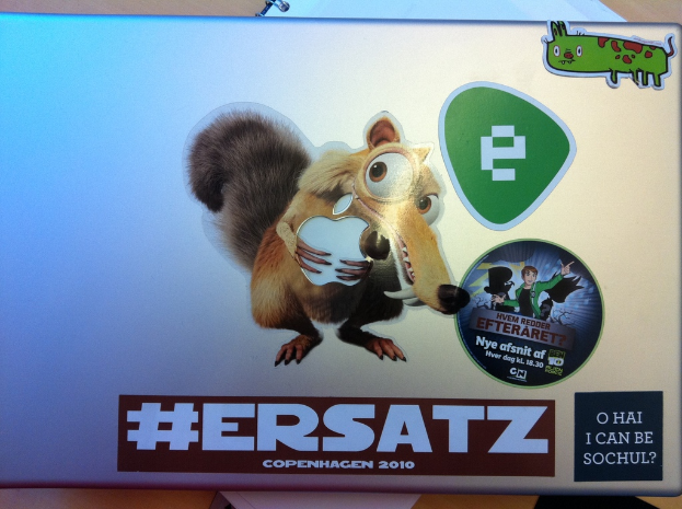 Ein Laptop und ein Buch auf einem Tisch, mit verschiedenen Aufklebern auf dem Laptop.