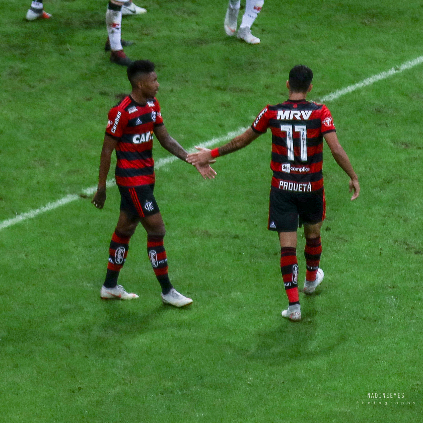 Zwei Fußballspieler in gestreifter Uniform schütteln sich die Hände auf einem grünen Feld und lächeln.