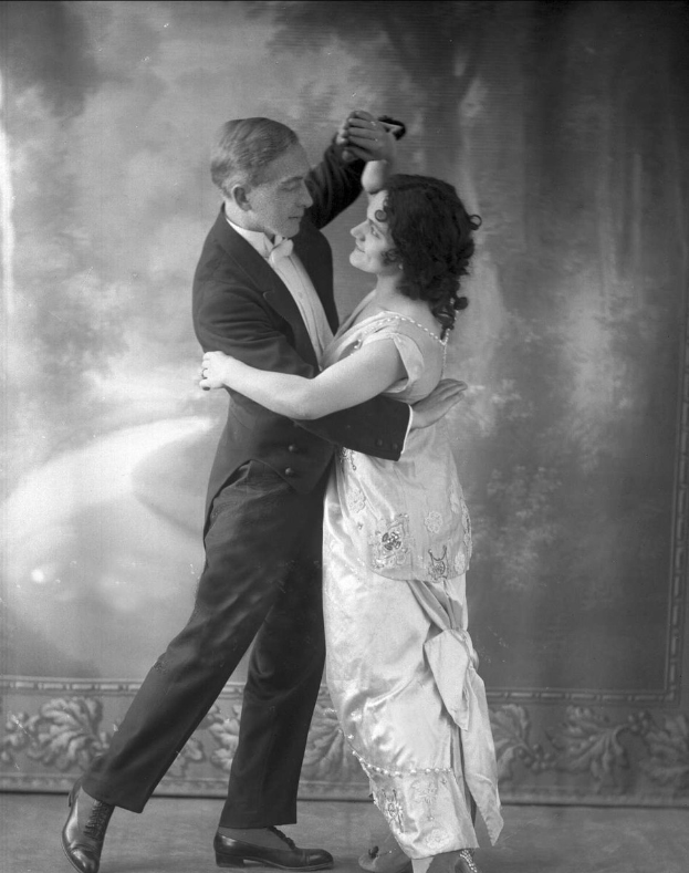 Altes Schwarz-Weiß-Foto eines Mannes in einem Anzug und einer Frau, die Tango tanzen, mit aufwändigen Wanddesigns im Hintergrund.